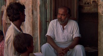Movie still from “Salaam Bombay!” (1988), directed by Mira Nair – A man sitting on the ground talking to two other people; Medium shot, Over the shoulder angle