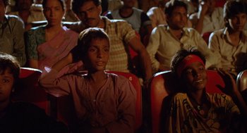 Movie still from “Salaam Bombay!” (1988), directed by Mira Nair – A group of people sitting in a room watching a movie; Close Up shot, High angle