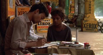 Movie still from “Salaam Bombay!” (1988), directed by Mira Nair – A young man is writing on a piece of paper while a young boy looks on; Medium shot, High angle