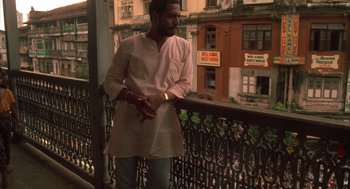 Movie still from “Salaam Bombay!” (1988), directed by Mira Nair – A man standing on a balcony looking out at a city; Medium shot, Low angle