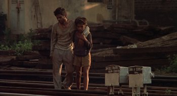 Movie still from “Salaam Bombay!” (1988), directed by Mira Nair – A man and a child walking on a train track; Wide shot, High angle