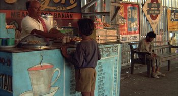 Movie still from “Salaam Bombay!” (1988), directed by Mira Nair – A young boy standing in front of a counter; Wide shot, High angle