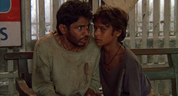 Movie still from “Salaam Bombay!” (1988), directed by Mira Nair – Two young men are sitting together and one has his arm wrapped around the shoulder of the other man; Medium shot, High angle