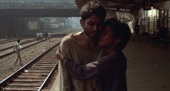 Movie still from “Salaam Bombay!” (1988), directed by Mira Nair – A man and a woman hugging on a train track; Medium shot, High angle