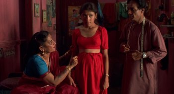 Movie still from “Salaam Bombay!” (1988), directed by Mira Nair – A woman in a red dress is getting ready for a photo; Medium shot, High angle