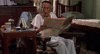 Movie still from “Salaam Bombay!” (1988), directed by Mira Nair – An older man sitting in a chair reading a newspaper; Medium shot, High angle