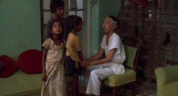 Movie still from “Salaam Bombay!” (1988), directed by Mira Nair – An old man sitting on a chair with three young children; Medium shot, Low angle