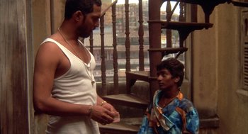 Movie still from “Salaam Bombay!” (1988), directed by Mira Nair – A man standing next to a young boy holding money; Medium shot, High angle