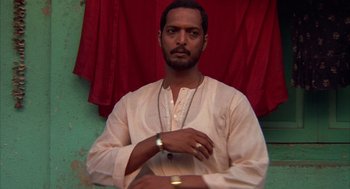 Movie still from “Salaam Bombay!” (1988), directed by Mira Nair – A man in a white shirt and a red curtain; Close Up shot, Low angle