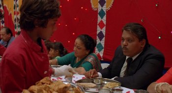 Movie still from “Salaam Bombay!” (1988), directed by Mira Nair – A group of people sitting at a table with plates of food on it; Medium shot, Over the shoulder angle