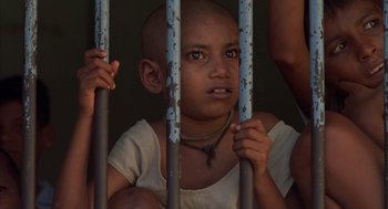 Movie still from “Salaam Bombay!” (1988), directed by Mira Nair – A young child is holding onto a metal bar; Close Up shot, High angle