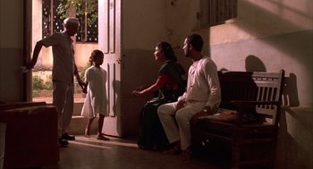 Movie still from “Salaam Bombay!” (1988), directed by Mira Nair – A man and a woman sitting next to each other in front of a door; Wide shot, High angle