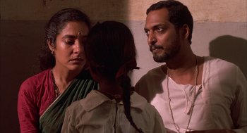 Movie still from “Salaam Bombay!” (1988), directed by Mira Nair – A man and a woman standing next to a young girl; Close Up shot, Over the shoulder angle