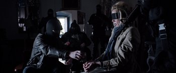 Movie still from “Salt and Fire” (2016), directed by Werner Herzog – Blindfolded people in a dark room with a man holding a cigarette; Medium shot, Over the shoulder angle