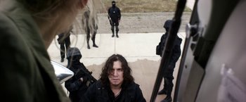 Movie still from “Salt and Fire” (2016), directed by Werner Herzog – A group of men standing around a building with guns; Medium shot, Over the shoulder angle