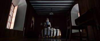 Movie still from “Salt and Fire” (2016), directed by Werner Herzog – A woman sitting on top of a bed in a dark room; Wide shot, Low angle