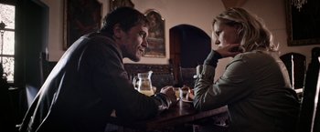 Movie still from “Salt and Fire” (2016), directed by Werner Herzog – A man and a woman sitting at a wooden table; Medium shot, Over the shoulder angle