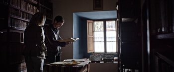 Movie still from “Salt and Fire” (2016), directed by Werner Herzog – A man standing in front of a window reading a book; Medium shot, Low angle