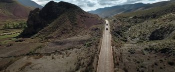 Movie still from “Salt and Fire” (2016), directed by Werner Herzog – Two cars driving down a dirt road on a cloudy day; Extreme Wide shot, High angle