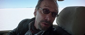 Movie still from “Salt and Fire” (2016), directed by Werner Herzog – A person wearing glasses and a jacket; Close Up shot, Low angle