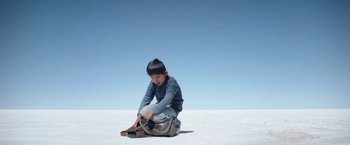 Movie still from “Salt and Fire” (2016), directed by Werner Herzog – A young boy sitting on the ground with a skateboard; Wide shot, Low angle