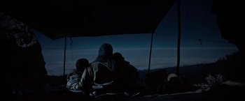 Movie still from “Salt and Fire” (2016), directed by Werner Herzog – A group of people sitting under an umbrella at night; Wide shot, Low angle