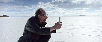 Movie still from “Salt and Fire” (2016), directed by Werner Herzog – A man is taking a picture with a cell phone; Close Up shot, Low angle