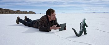 Movie still from “Salt and Fire” (2016), directed by Werner Herzog – A man laying on the ground looking at an ipad; Medium shot, High angle