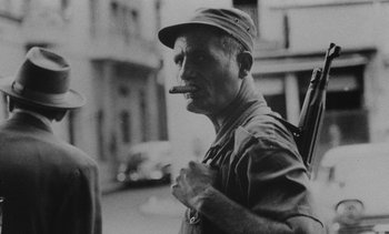 Movie still from “Salut les Cubains” (1963), directed by Agnès Varda – An older man smoking a cigar while standing on the side of the road; Close Up shot, Low angle