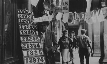 Movie still from “Salut les Cubains” (1963), directed by Agnès Varda – An old man standing in front of a store with a bunch of signs; Wide shot, High angle