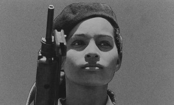 Movie still from “Salut les Cubains” (1963), directed by Agnès Varda – A black and white photo of a woman holding a rifle; Close Up shot, Low angle