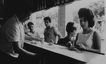 Movie still from “Salut les Cubains” (1963), directed by Agnès Varda – A group of people sitting at a table in a restaurant; Medium shot, Low angle