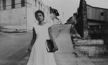 Movie still from “Salut les Cubains” (1963), directed by Agnès Varda – A black and white photo of a woman holding a book; Medium shot, Low angle