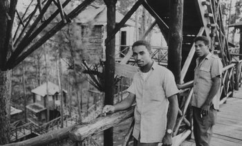 Movie still from “Salut les Cubains” (1963), directed by Agnès Varda – A black and white photo of a man standing next to a wooden fence; Medium shot, High angle