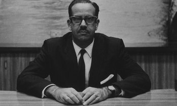 Movie still from “Salut les Cubains” (1963), directed by Agnès Varda – A man sitting at a table wearing a suit and tie; Close Up shot, Low angle