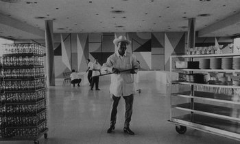 Movie still from “Salut les Cubains” (1963), directed by Agnès Varda – A man holding a baseball bat while standing in a room; Wide shot, Low angle