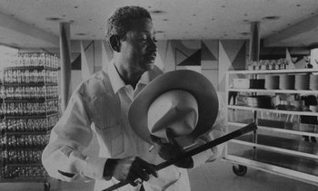 Movie still from “Salut les Cubains” (1963), directed by Agnès Varda – A black and white photo of a man holding a hat; Medium shot, Low angle