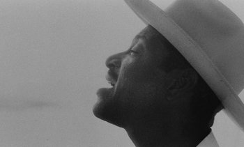 Movie still from “Salut les Cubains” (1963), directed by Agnès Varda – A black and white photo of a man wearing a white hat; Extreme Close Up shot, Low angle