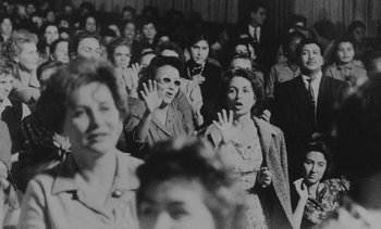 Movie still from “Salut les Cubains” (1963), directed by Agnès Varda – A group of people standing in a room with their hands up; Medium shot, High angle