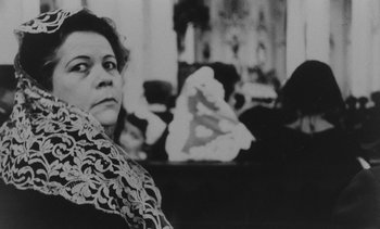 Movie still from “Salut les Cubains” (1963), directed by Agnès Varda – An older woman sitting in front of a painting; Close Up shot, Low angle
