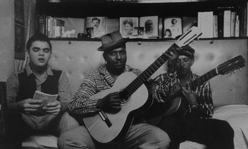 Movie still from “Salut les Cubains” (1963), directed by Agnès Varda – A black and white photo of a man holding a guitar; Medium shot, Low angle
