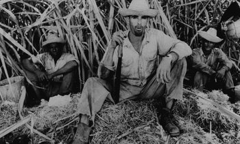 Movie still from “Salut les Cubains” (1963), directed by Agnès Varda – A man sitting on top of a pile of hay next to another man; Medium shot, High angle