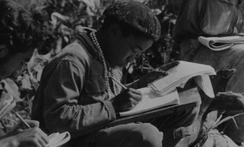 Movie still from “Salut les Cubains” (1963), directed by Agnès Varda – An old black and white photo of a person writing; Close Up shot, High angle
