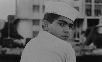 Movie still from “Salut les Cubains” (1963), directed by Agnès Varda – A young man in a sailor's uniform looks to his left; Close Up shot, Low angle