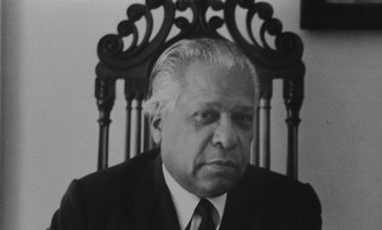Movie still from “Salut les Cubains” (1963), directed by Agnès Varda – An older man wearing a suit sitting in a chair; Close Up shot, Low angle