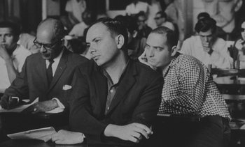 Movie still from “Salut les Cubains” (1963), directed by Agnès Varda – A black - and - white photo of a man sitting in a crowd; Medium shot, Low angle