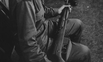 Movie still from “Salut les Cubains” (1963), directed by Agnès Varda – A man sitting down holding a rifle in his hands; Extreme Close Up shot, High angle