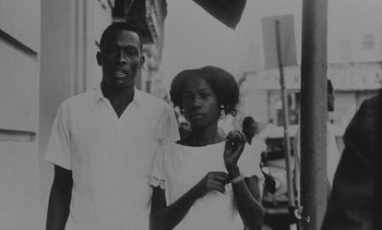 Movie still from “Salut les Cubains” (1963), directed by Agnès Varda – A man and a woman standing next to each other on the street; Close Up shot, Low angle