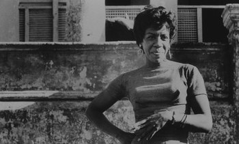 Movie still from “Salut les Cubains” (1963), directed by Agnès Varda – An old black and white photo of a woman in front of a building; Medium shot, Low angle