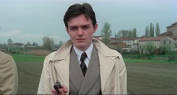Movie still from “Salò, or the 120 Days of Sodom” (1975), directed by Pier Paolo Pasolini – A man in a trench coat and tie holding a camera; Close Up shot, Low angle